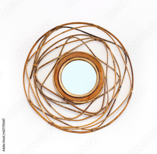 Round mirror in wide wicker rattan frame on white wall, decor element for home interior in colonial style. Handmade rattan weaving furniture from twisted twigs.