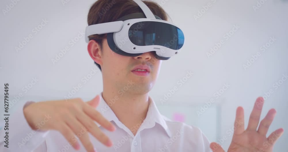 Young asian businessman wearing VR and using to work. He using hand to control data while wearing VR goggles. Young asian businessman wearing VR and using to work. He using hand to control data while wearing VR goggles.