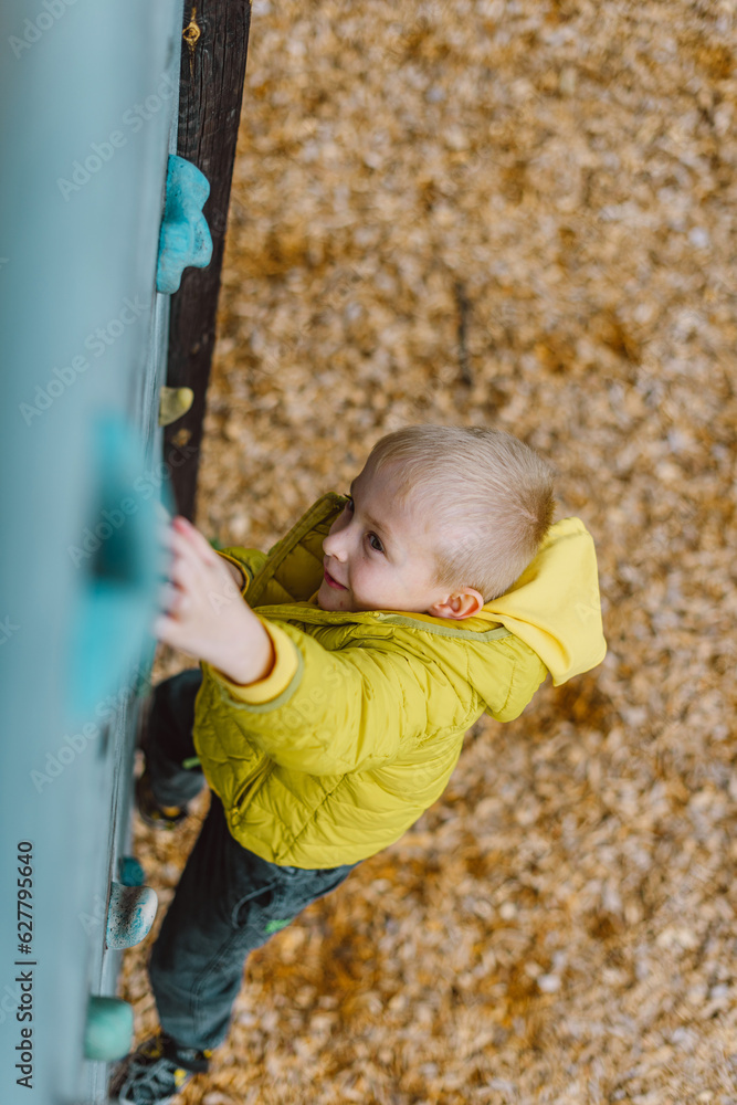 Boy At The Climbing Wall Without A Helmet, Danger At The Climbing Wall. Little Boy Climbing A Rock Wall Indoor Boy At The Climbing Wall Without A Helmet, Danger At The Climbing Wall. Little Boy Climbing A Rock Wall Indoor