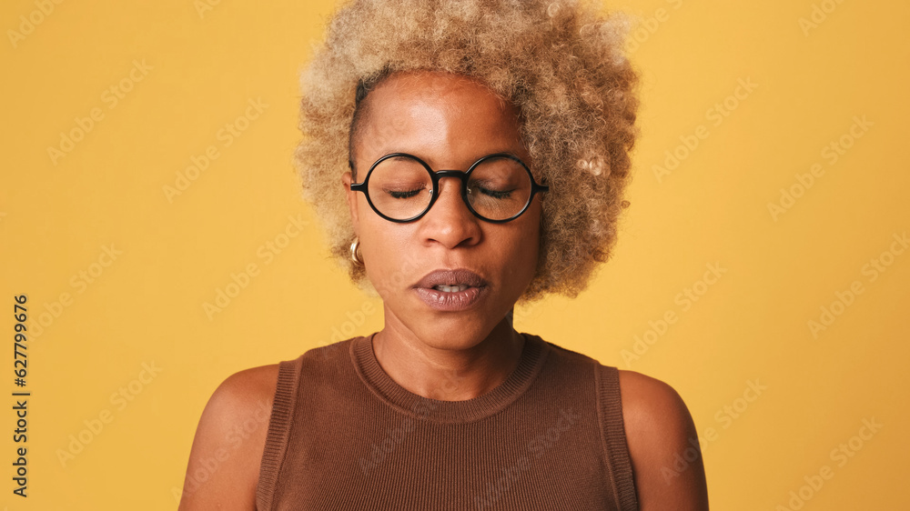 Close-up of bored, dissatisfied girl in glasses, wearing brown top sighs closes eyes, not happy with the situation isolated on orange background Close-up of bored, dissatisfied girl in glasses, wearing brown top sighs closes eyes, not happy with the situation isolated on orange background