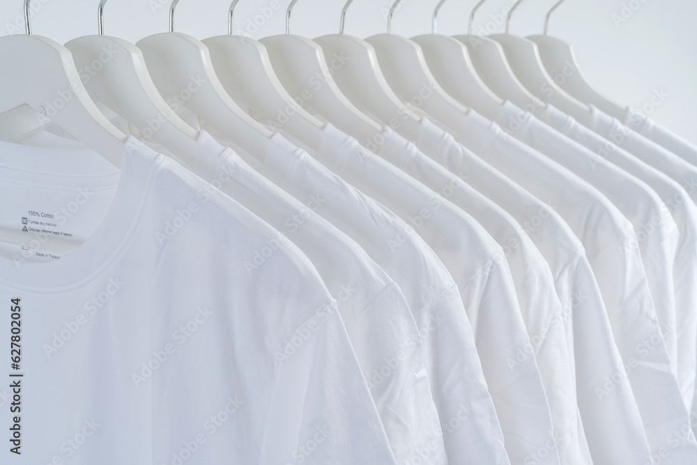 Fototapeta premium Close-up of white t-shirts on hangers, a collection of white t-shirts hang on a wooden clothes hanger