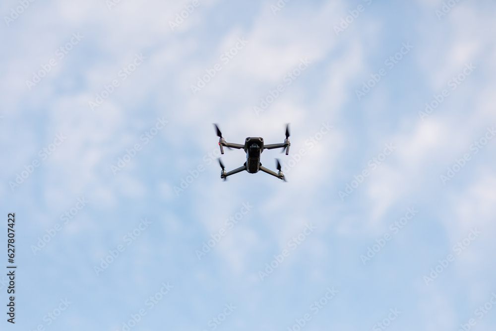 Fototapeta premium Drone flying on blue sky with white clouds background. Bottom view Quadcopter with digital camera. Flying remote control Quadrocopter, UAV.