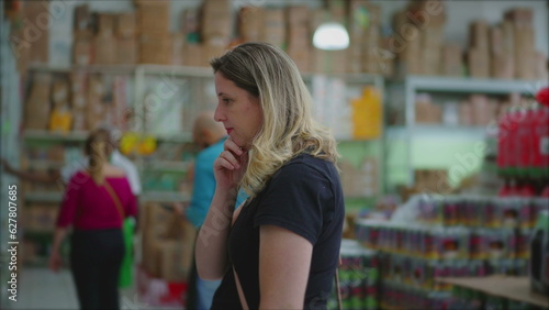 Female consumer looking for products on shelf at grocery store, considering merchandise for sale, pondering decision, consumerism lifestyle habits