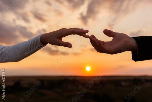 Fotobehang Hands of bride and groom reaching each other, touching fingers on sunset sky countryside background