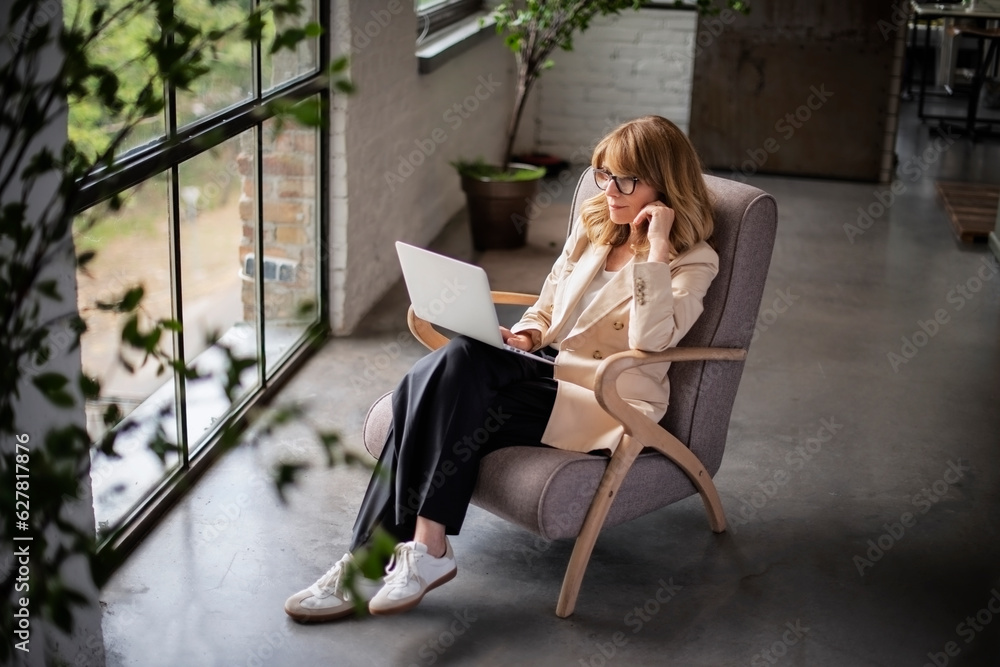High angle shot of mid aged woman sitting in an armchair and using laptop at home High angle shot of mid aged woman sitting in an armchair and using laptop at home