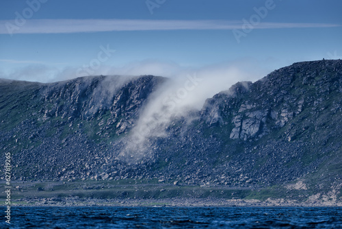 Fototapeta Naklejka Na Ścianę i Meble -  Dramatic sea fog rising trough hole in a ridge in Knivskjelodden that the real northernmost point of Europe and close close to North Cape in August 2022.