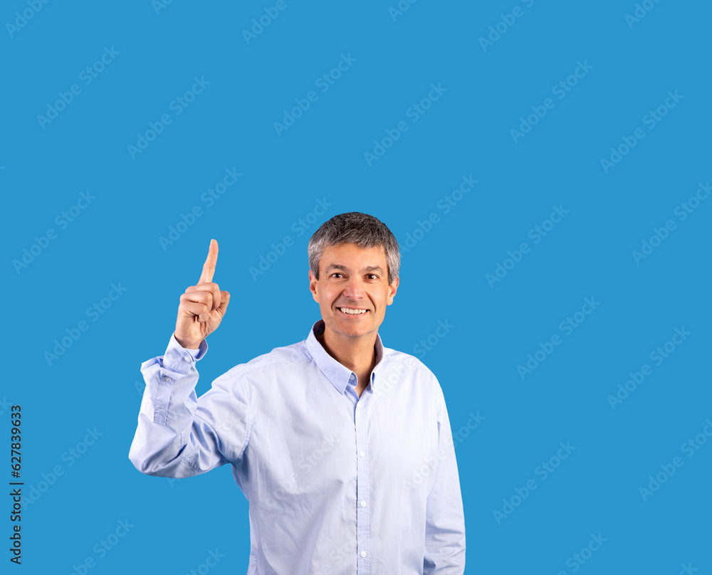 Happy mature man pointing finger up standing on blue background Happy mature man pointing finger up standing on blue background