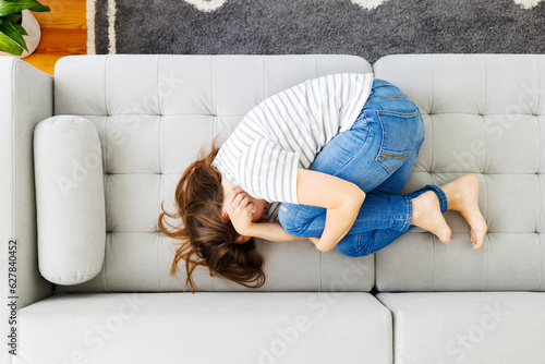 Tableau sur toile Frustrated woman covering face and crying, lying on sofa at home alone
