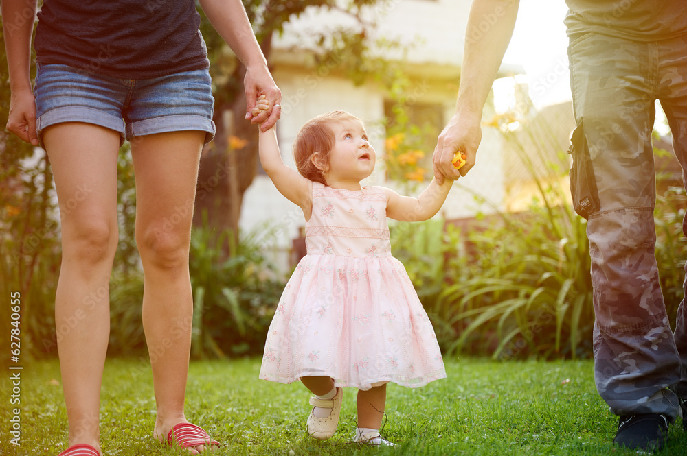 Lovely family walking holding hands, adopted child being supported by loving parents. Girl holds hands of her parents and jumps. Cropportrait of the cute adorable small girl in dress. Lovely family walking holding hands, adopted child being supported by loving parents. Girl holds hands of her parents and jumps. Cropportrait of the cute adorable small girl in dress.