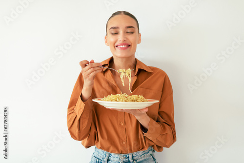 Satisfied caucasian lady enjoying tasty Italian spaghetti with closed eyes, standing on white studio background wall