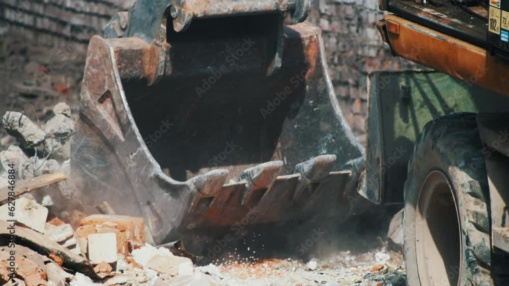 Black excavator bucket working on construction site or demolition building, raking crushed bricks and rubbish. Close-up view, summer, daylight. Heavy building machinery operating Black excavator bucket working on construction site or demolition building, raking crushed bricks and rubbish. Close-up view, summer, daylight. Heavy building machinery operating