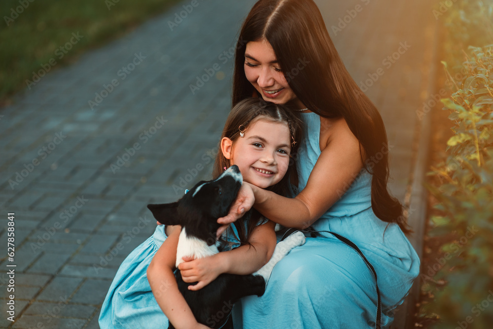 Happy family mother daughter and funny puppy hugging in the park. Family portrait. Happy motherhood and childhood Happy family mother daughter and funny puppy hugging in the park. Family portrait. Happy motherhood and childhood