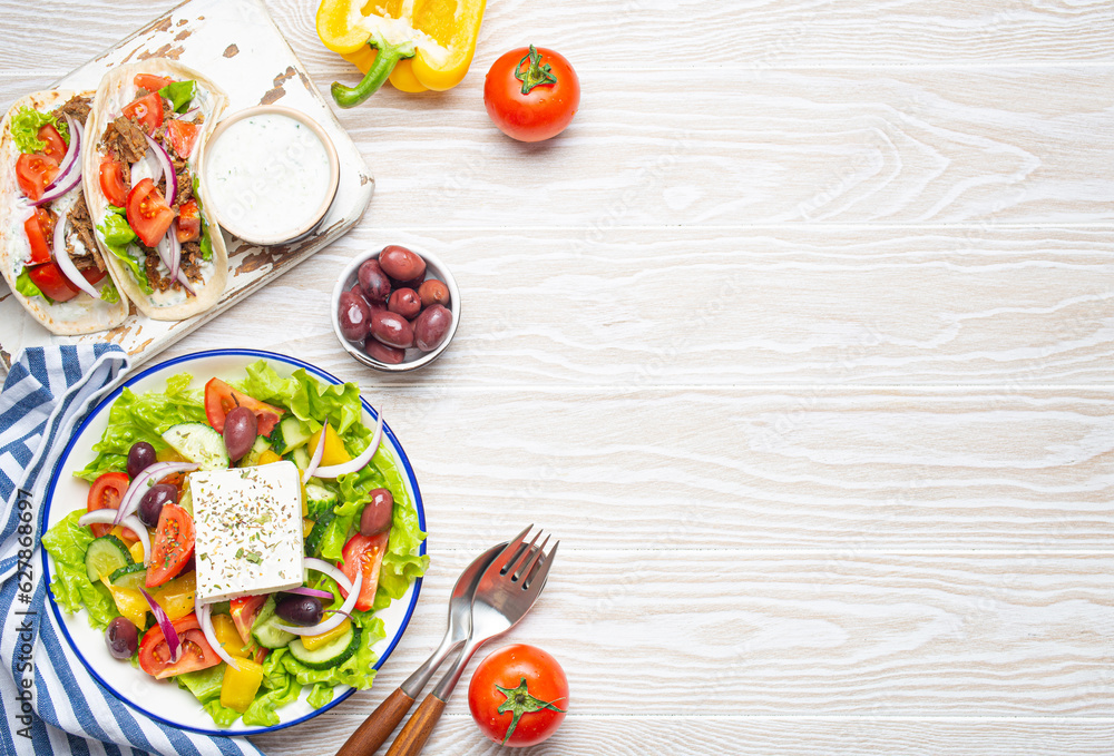 Traditional Greek Food: Greek Salad, Gyros with meat and vegetables, Tzatziki sauce, Olives on White rustic wooden table background from above. Cuisine of Greece. Copy space Traditional Greek Food: Greek Salad, Gyros with meat and vegetables, Tzatziki sauce, Olives on White rustic wooden table background from above. Cuisine of Greece. Copy space