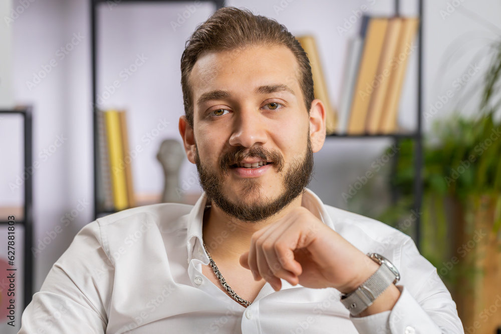 Naklejka premium Portrait of happy smiling bearded middle eastern businessman at modern home office workplace desk looking at camera. Male in formal shirt. Man guy remote distant online working on laptop