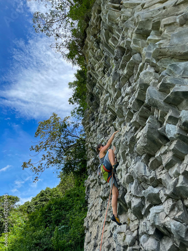 Incredible climbing wall with volcanic rock and young woman in middle of climb