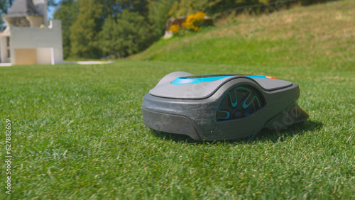 CLOSE UP, DOF: Modern robotic lawn mower trimming green garden turf autonomously