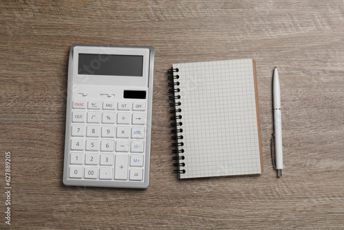 Calculator and office stationery on wooden table, flat lay. Space for text