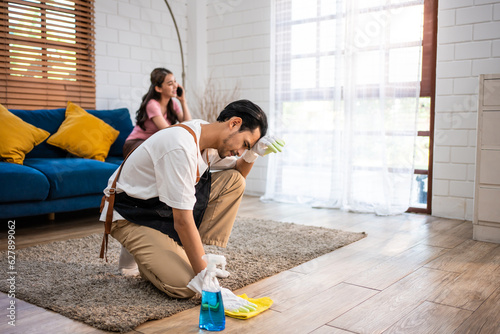 Asian young man cleaning house indoors following order from his wife. 