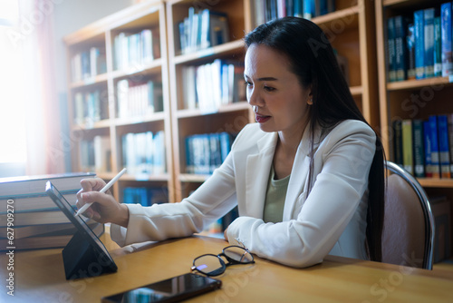 Female university lecturer working in library with a tablet and books on table © EduLife Photos