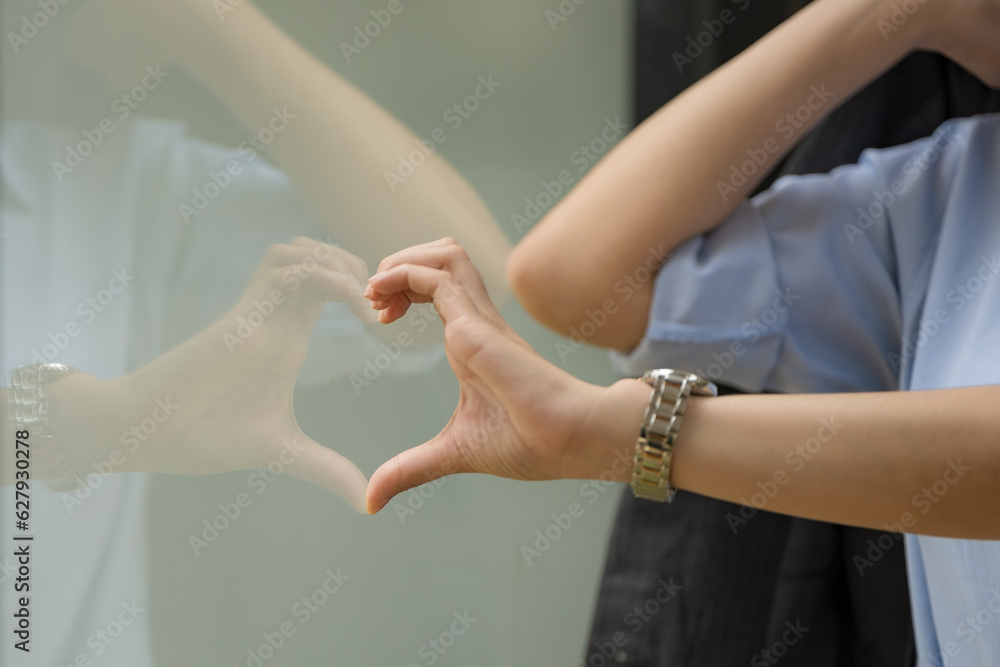 Fototapeta premium Close-up hand of Asian businesswoman to heart shape with window glass.