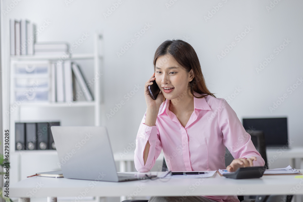 Asian Woman entrepreneur busy with her work in the office. Young Asian woman talking over smartphone or cellphone while working on computer at her desk.
Asian Woman entrepreneur busy with her work in the office. Young Asian woman talking over smartphone or cellphone while working on computer at her desk.