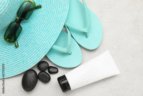 Composition with hat, sunglasses, flip flops, pebbles and bottle of sunscreen on light background