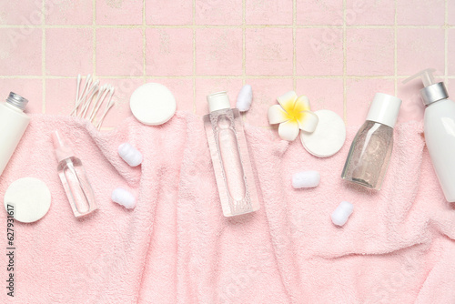 Towel with micellar water, cotton pads, buds, balls and flower on pink tile background
