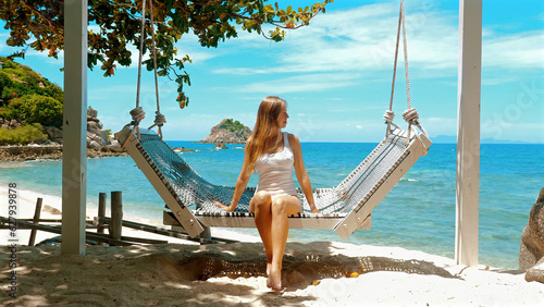 Woman sitting on hammock at tropical beach. Concept of a carefree summer escape.