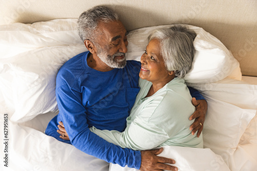 Happy senior biracial couple lying in bed and embracing at home