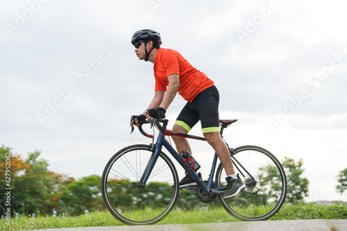 Young guy wearing sport clothing, Cyclist pedaling on a racing bike outdoors in a sunny day