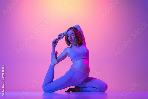 Fototapeta Naklejka Na Ścianę i Meble -  Pregnant woman doing legs stretching yoga exercises in neon