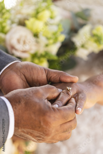 Hands of senior biracial groom putting wedding ring on finger of his bride
