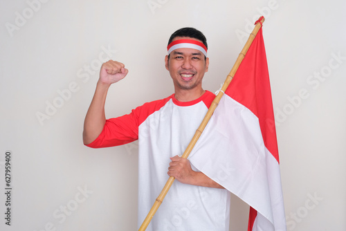 Indonesian man smiling and clenching fist while holding country flag photo