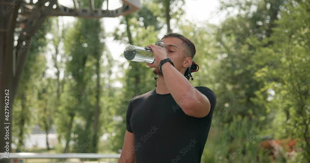 Tired exhausted dehydrated african american athlete man runner drinking water from sports bottle after jogging at city park