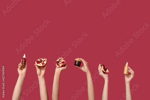 Female hands holding cosmetic products and pomegranate on red background