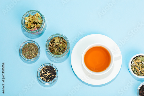 Beautiful composition of green and black tea leaves in glass small jars and white ceramic cup of hot tea from above on light background. Morning rituals.
