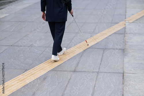 Tablou pe pânză Close-up of the legs of a blind businesswoman walking along a tactile tile with a cane