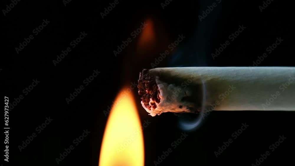 Lighting up cigarette with fire flame in black background. Smoking