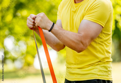 Man excercising with elastic rubber band outdoors making arm workout. Guy making fitness with sport equipment and training stretght