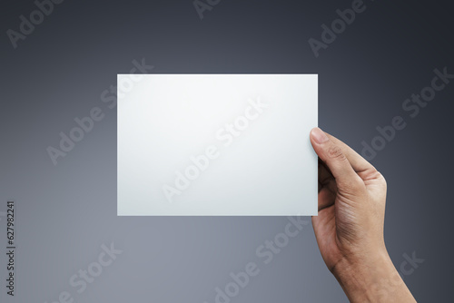 Woman hand holding a blank paper on gray background.
