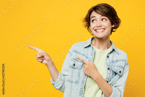 Young happy woman she wear green t-shirt denim shirt casual clothes point index finger aside indicate on workspace area copy space mock up isolated on plain yellow background studio Lifestyle concept photo