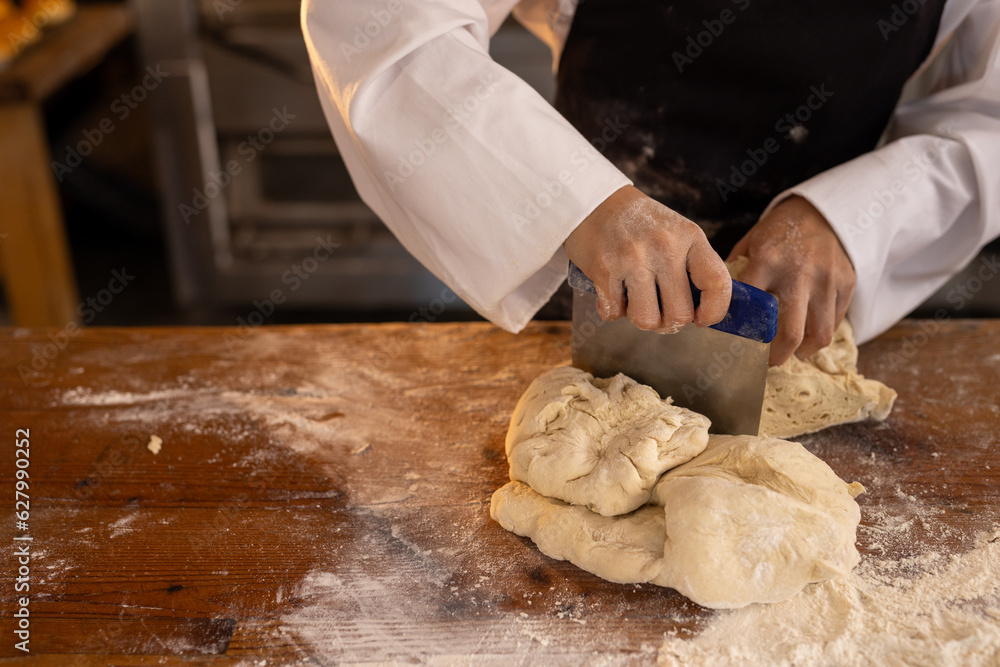 Asian female baker wearing apron in bakery kitchen and cutting dough, copy space Asian female baker wearing apron in bakery kitchen and cutting dough, copy space