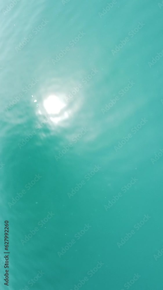Vertical aerial view on sea water surface, camera flies over clear sea water. Sun glare. Abstract nautical summer ocean nature. Holiday, vacation and travel concept. Nobody. Vertical video Vertical aerial view on sea water surface, camera flies over clear sea water. Sun glare. Abstract nautical summer ocean nature. Holiday, vacation and travel concept. Nobody. Vertical video