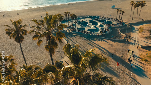 Skateboarders enjoying the sunset at a popular beach skate park surrounded by palm trees in Venice Beach, California during a vibrant evening