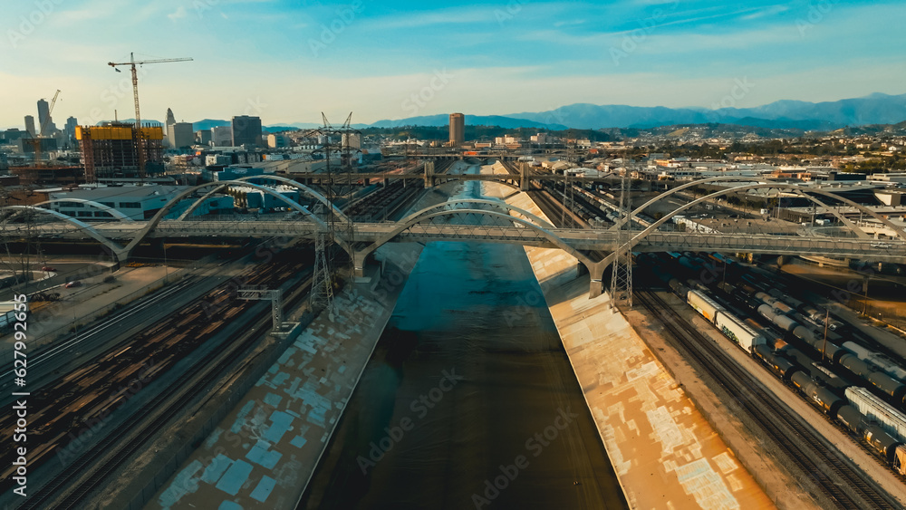 Fototapeta premium Urban landscape showing train tracks and bridges alongside a waterway in a bustling city at sunset