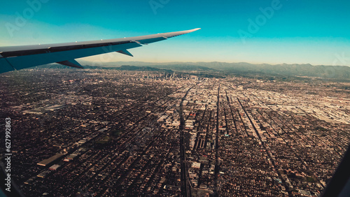View of a sprawling urban landscape with mountains visible on the horizon taken from an airplane wing during daytime
