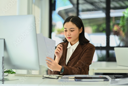 Photo of young businesswoman in stylish suit working with financial reports at desk
