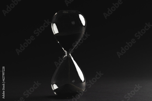 Close up of hourglass with black sand and copy space on black background