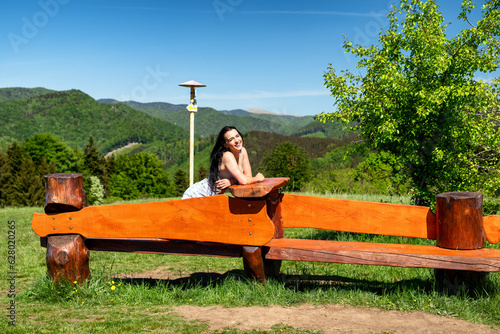 Brunette girl sitting on the wooden bench in beautiful summer country