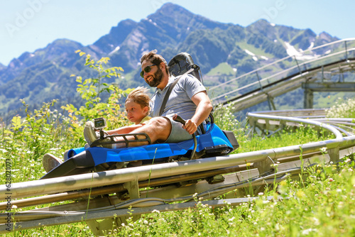 Obraz na plátně father and child having ride on summer toboggan called Rodelbahn rushing down the track